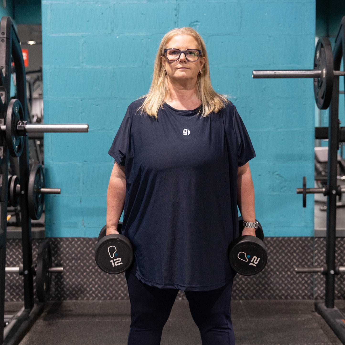 Plus size woman wearing Gym Stuff Plus navy activewear lifting dumbbells in gym, showing supportive comfortable fit for confident workouts.