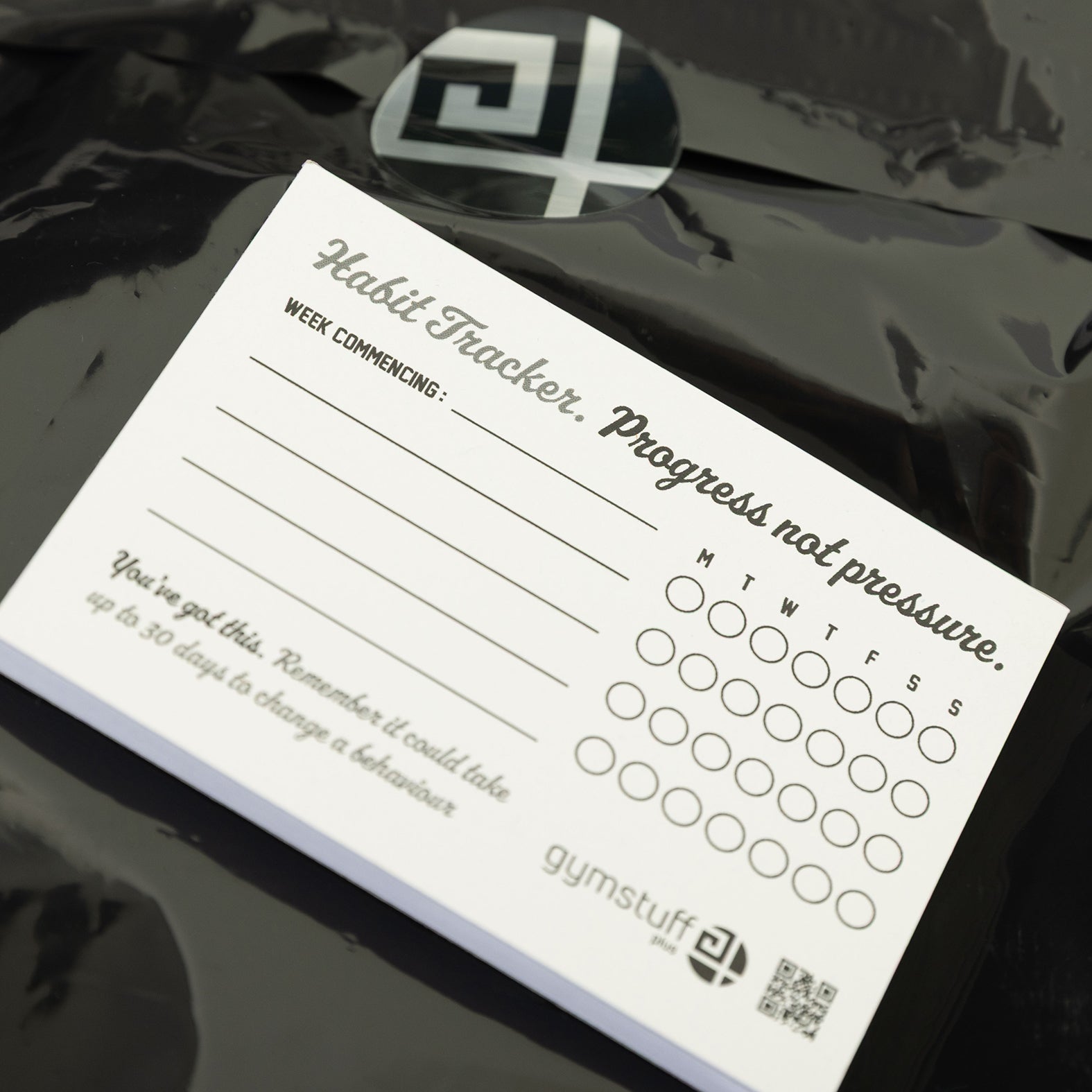 Gym Stuff Plus habit tracker pad with text 'Progress not pressure' on top of branded packaging, supporting plus size women’s fitness motivation.